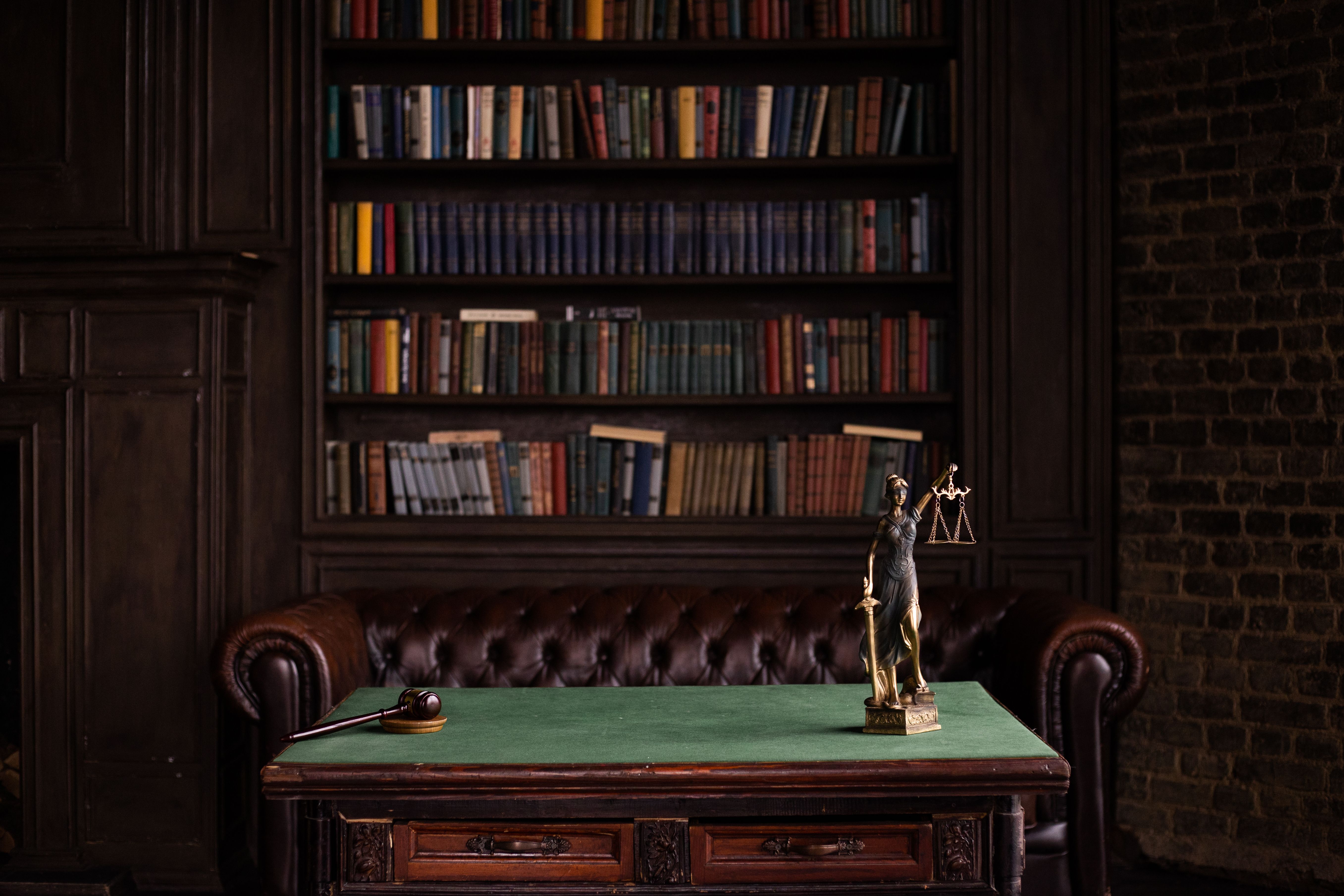 A classic study room with shelves of law books, a gavel, and a Lady Justice figurine on a green table