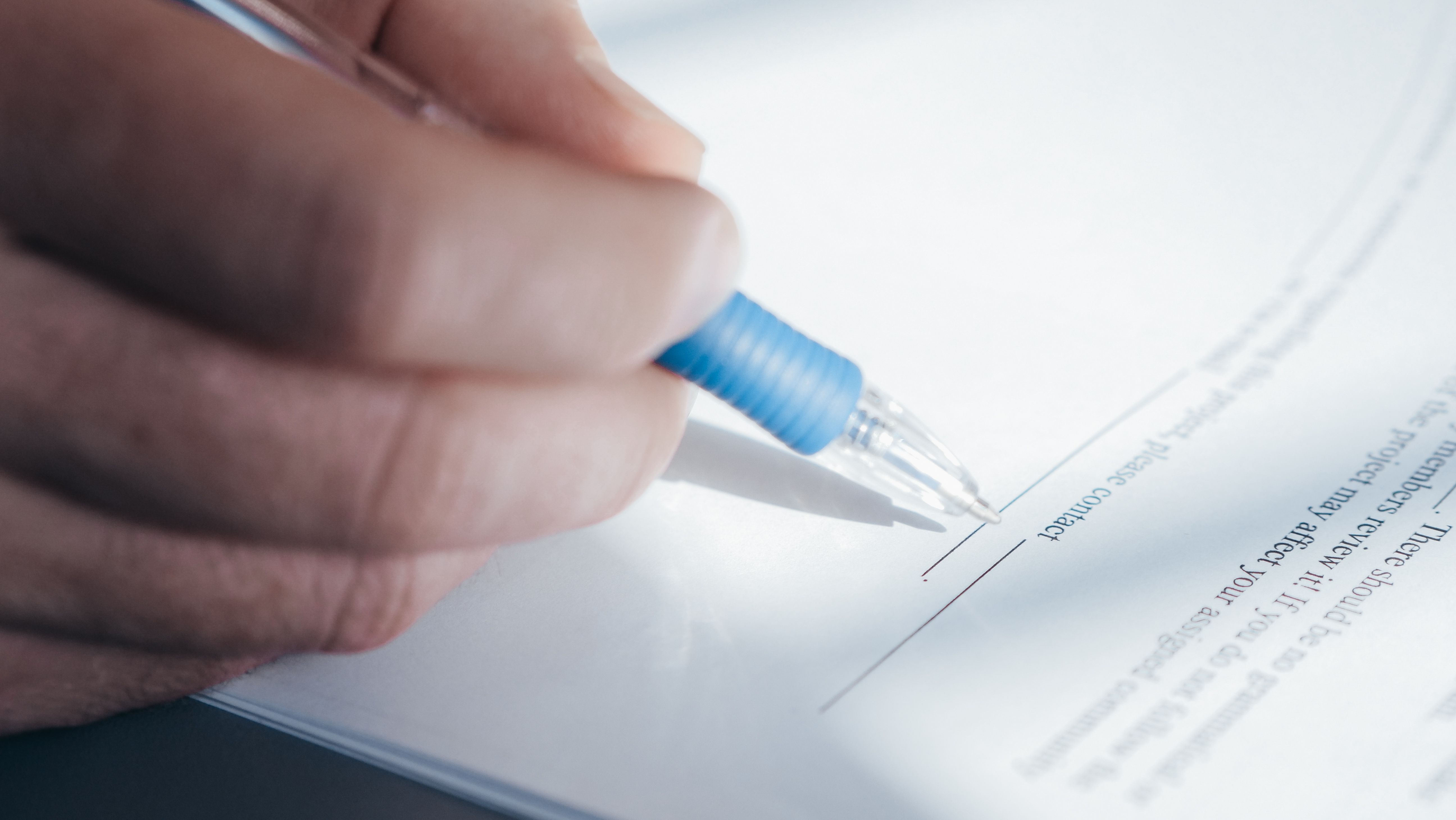 Close-up of a hand holding a pen signing a legal agreement