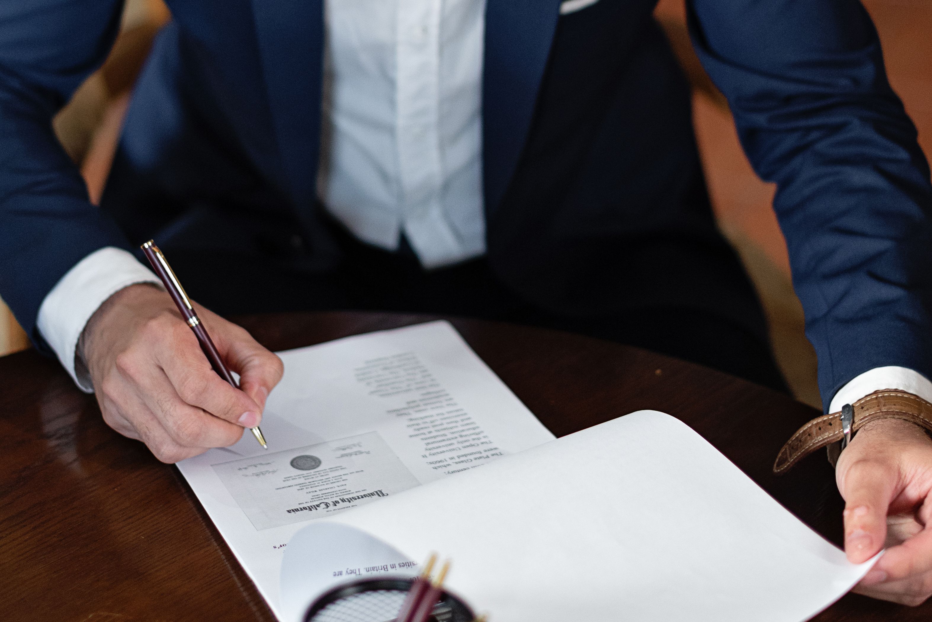 Professional signing legal documents at a desk, representing agreements that help creative businesses control risk and costs.