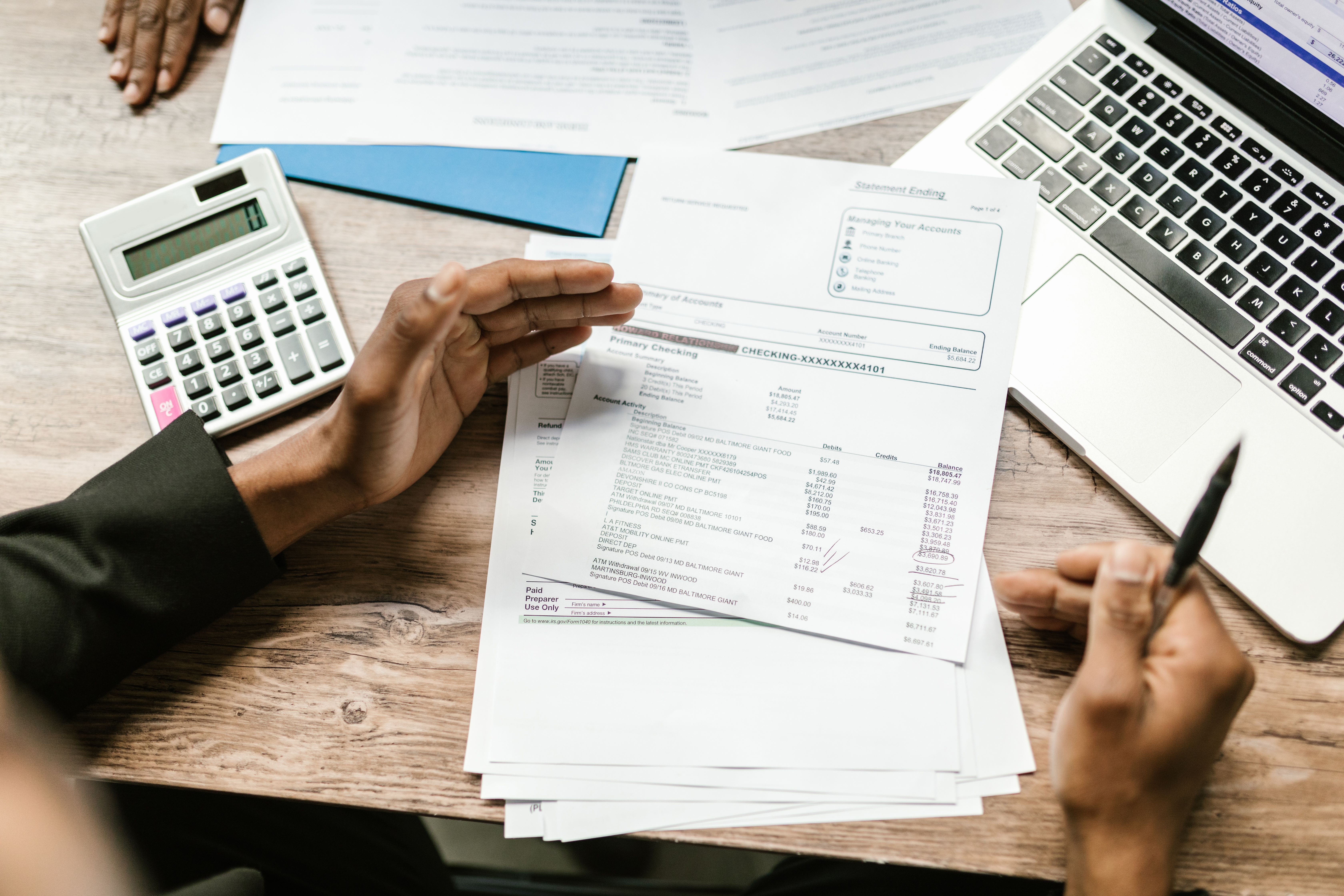 Hands reviewing financial documents beside a calculator and laptop, representing budgeting and tracking legal costs.